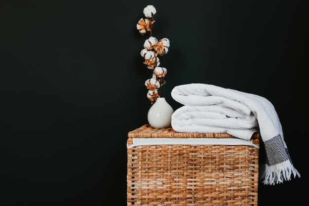 Photo serviettes en coton blanc sur une boîte en rotin avec une branche de cooton contre un mur noir dans une blanchisserie