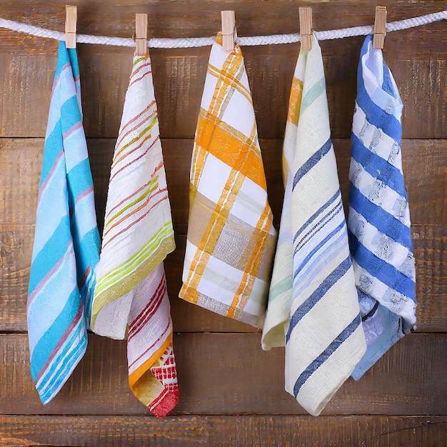 Des serviettes de cuisine pliées colorées accrochées à une corde sur un fond en bois