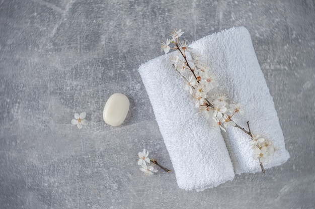 Serviettes douces roulées avec des branches de cerisier en fleurs et du savon sur fond gris clair. Concept de SPA. Minimalisme, flou artistique, vue de dessus.