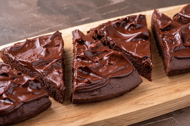 Servir un brownie triangulaire avec de la crème de ganache sur une planche de bois. Fermer.