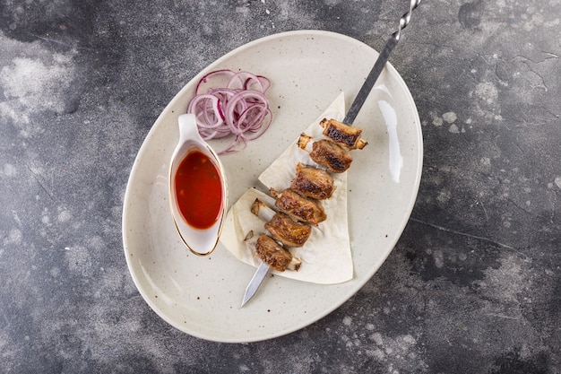 Servir dans un restaurant sur une assiette blanche de brochettes de porc aromatiques sur des côtes avec sauce rouge et oignons hachés.