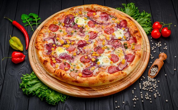 Servir de délicieuses pizzas avec des œufs de caille, des saucisses de jambon et des légumes sur fond noir