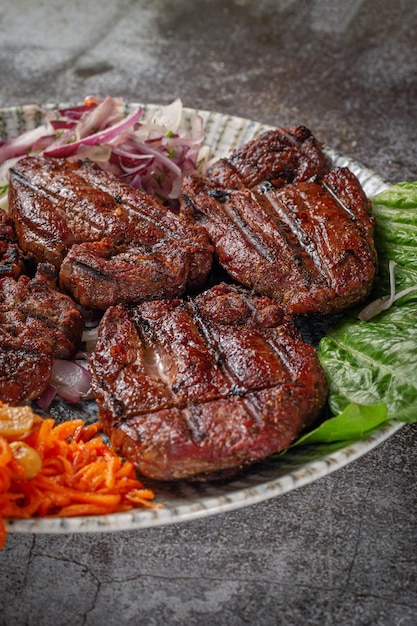 Servir un plat de la carte du restaurant. Viande de boeuf et de porc grillée avec carottes râpées et herbes sur une assiette contre une table en pierre grise, délicieux kebab