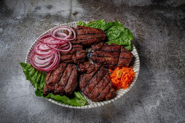 Servir un plat de la carte du restaurant. Viande de boeuf et de porc grillée avec carottes râpées et herbes sur une assiette contre une table en pierre grise, délicieux kebab