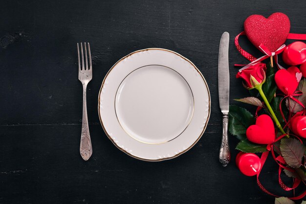 Servir la table pour célébrer la Saint-Valentin. Couverts, assiette, roses. Sur un fond en bois. Vue de dessus. Espace libre pour votre texte.