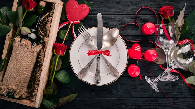 Servir la table pour célébrer la Saint-Valentin. Couverts, assiette, roses. Sur un fond en bois. Vue de dessus. Espace libre pour votre texte.