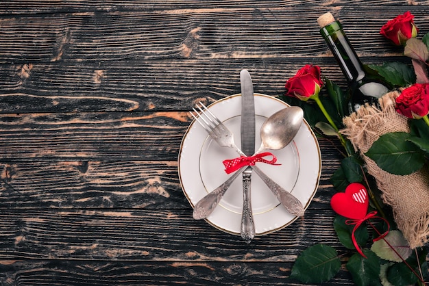 Servir la table pour célébrer la Saint-Valentin. Couverts, assiette, roses. Sur un fond en bois. Vue de dessus. Espace libre pour votre texte.