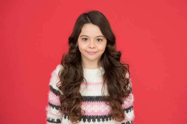 Photo ses cheveux sont coiffés de la meilleure façon possible. fille heureuse avec fond rouge de cheveux qui coule. petit sourire d'enfant aux cheveux ondulés. look beauté de petit modèle. salon de coiffure.