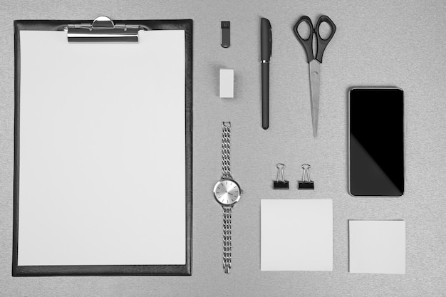 Set de bureau avec des feuilles blanches de papier, une montre de téléphone portable et de la papeterie sur un fond gris