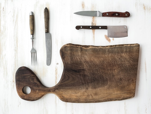 Set de cuisine. Vieille planche à découper rustique en bois de noyer, couteaux, fourchette sur un blanc