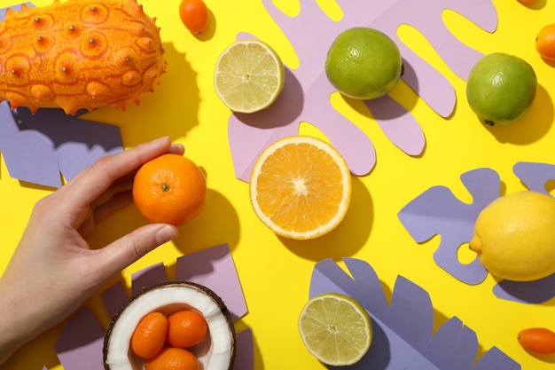 Photo set de fruits tropicaux à la main et de feuilles tropicales en papier sur fond jaune vue supérieure