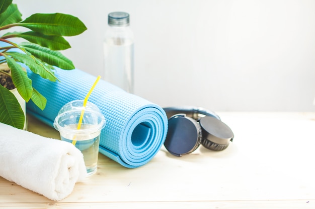 Set pour le sport. Des écouteurs de serviette de tapis de yoga bleu et une bouteille d'eau sur une lumière