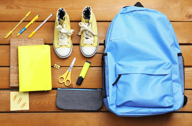 Set scolaire avec des chaussures et des fournitures de sac à dos sur fond de bois