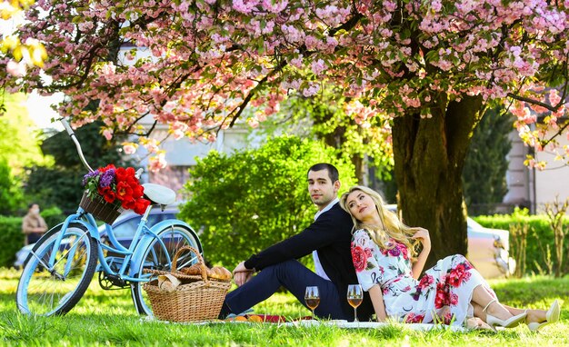 Seul l'amour peut nous réchauffer Couple de voyageurs romantiques sous un arbre en fleurs de sakura couple amoureux sur l'herbe verte profitant de la nature ensemble pique-niquer dans le parc de la ville homme et femme se détendre avec un panier alimentaire