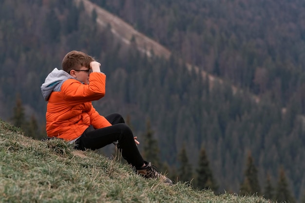 Seul garçon aux cheveux bruns veille sur la vallée et s'assoit sur la colline voyage randonnée voyage en plein air