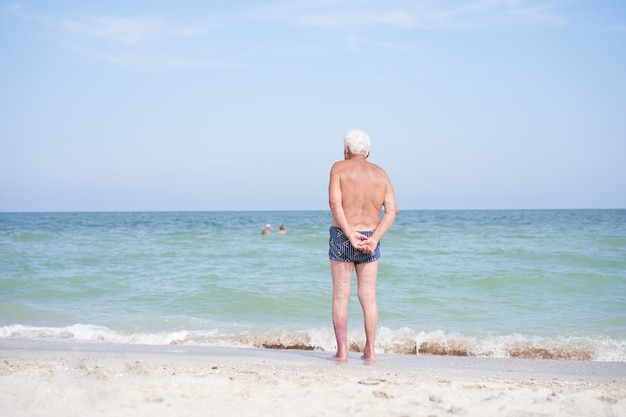 Seul homme senior debout sur la plage en regardant la mer
