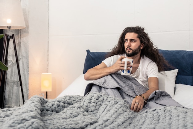 Seul à la maison. Agréable homme sérieux regardant la fenêtre tout en étant seul à la maison