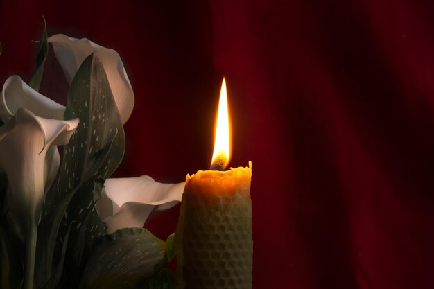 Photo une seule bougie de cire brûlante brûlant dans un environnement sombre contre un fond de rideau rouge près du lys de calla