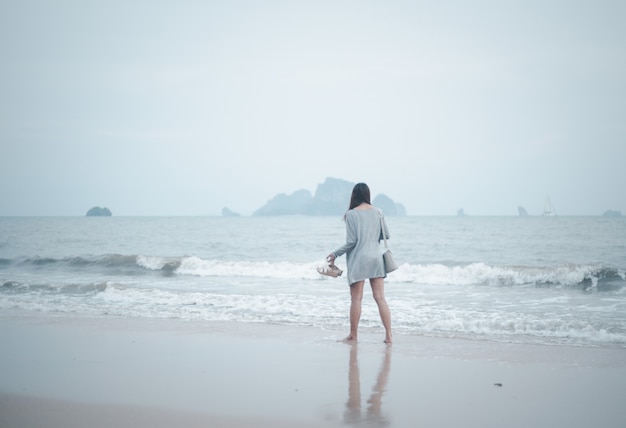 Seule femme marchant seule réfléchissant sur la surface de la plage sur un fond orageux sur la mer