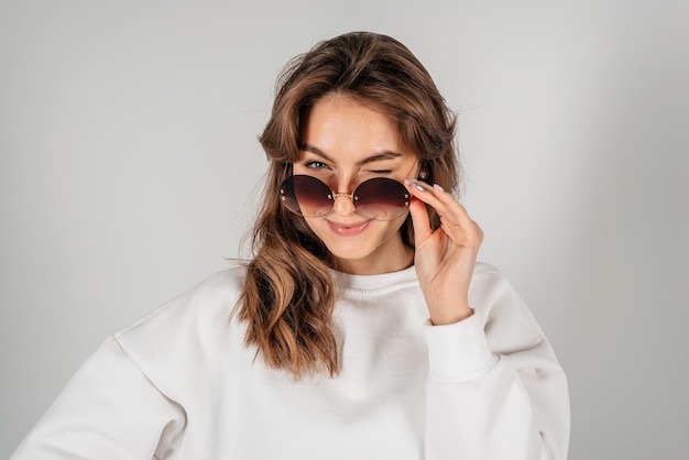 Sexy belle jeune femme à lunettes de soleil fashion posant et regardant sur fond blanc