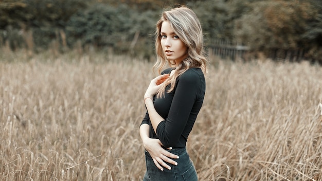 Sexy jeune femme dans une chemise noire debout dans un champ de maïs