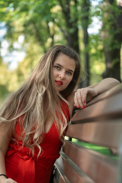 Sexy jeune femme en robe rouge avec de longs cheveux assis sur un banc dans le parc jolie fille cadre vertical