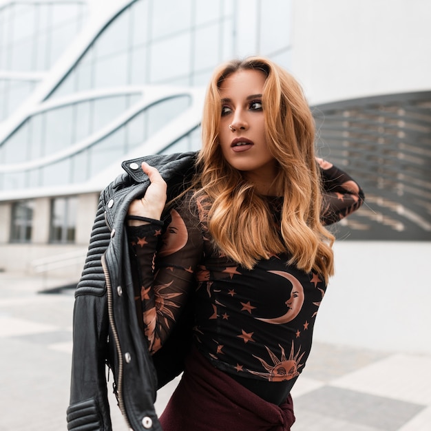 Sexy jeune femme rousse avec un beau maquillage avec une boucle d'oreille dans le nez dans une élégante veste en cuir noir dans une chemise vintage