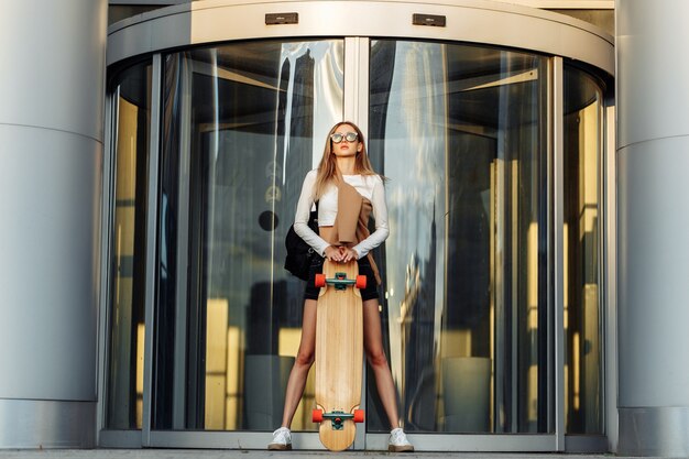 Sexy jeune femme skateboarder près du bâtiment en verre. Photo de haute qualité