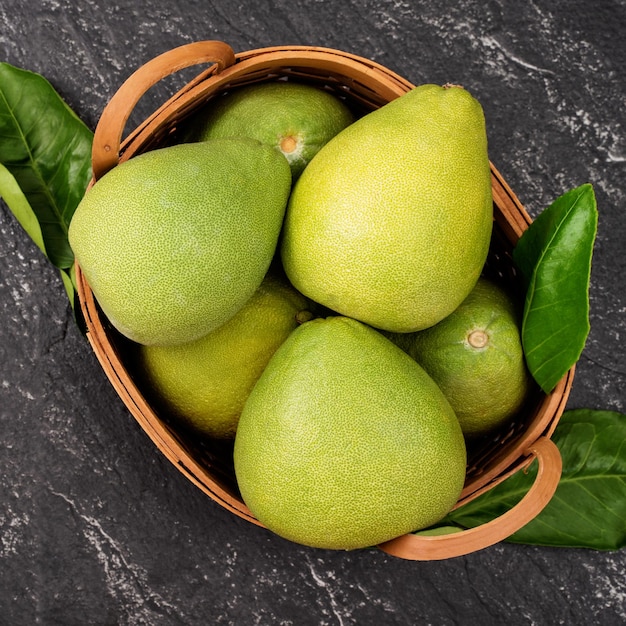 Shaddock pamplemousse pomelo pomelo frais dans panier en bambou avec des feuilles sur fond d'ardoise noir foncé Concept de fruits de saison Vue de dessus Mise à plat