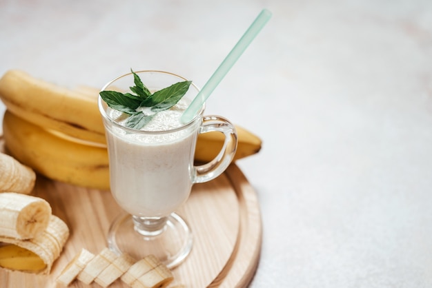 Shake de banane au lait décoré de feuilles de menthe dans un verre à latte avec poignée sur fond clair avec espace de copie, boissons d'été