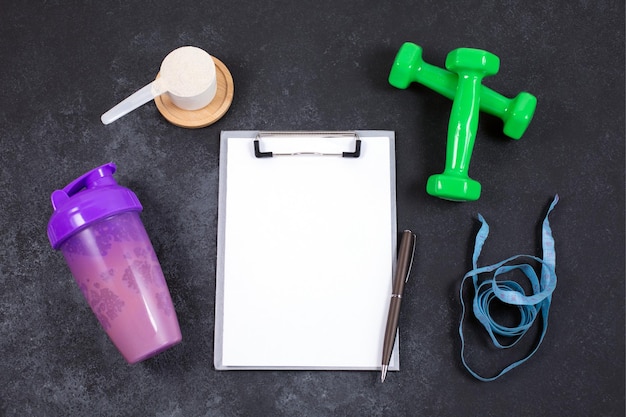 Photo shaker et cuillère à mesurer de ruban à mesurer d'haltères en poudre de protéines et cahier sur table sombre régime d'entraînement et de remise en forme concept de mode de vie sain