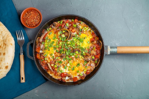 Photo shakshuka dans une poêle à frire sur fond gris à côté de légumes et de pain sur une serviette bleue