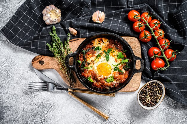 Shakshuka maison, œufs au plat, oignon, poivron, tomates et persil dans une casserole.