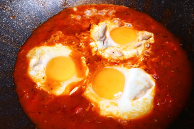 Photo shakshuka des œufs pochés dans une sauce tomate savoureuse pendant la cuisson dans une casserole en fonte