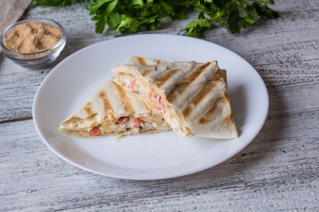 Shawarma dans du pain pita fin avec du poulet et des légumes sur une assiette blanche