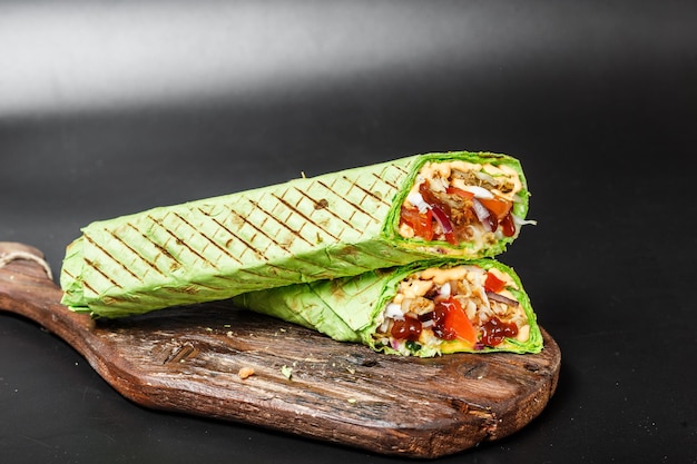 Shawarma égyptien dans du pain pita vert avec de la viande frite et des légumes sur une planche à découper en bois