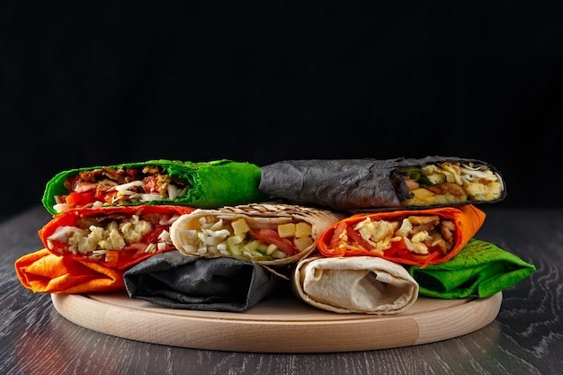 Le shawarma multicolore dans le pain pita est coupé et repose sur une surface en bois. Le plat du Moyen-Orient est préparé sur le grill et servi avec une sauce.