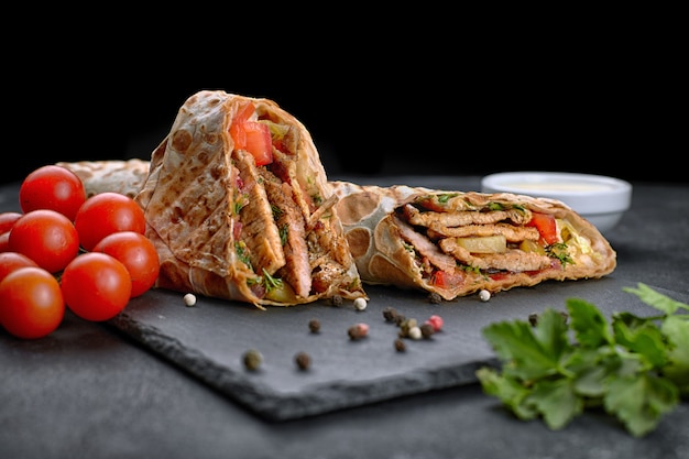 Shawarma de porc, sur fond noir, aux herbes, tomates et sauce