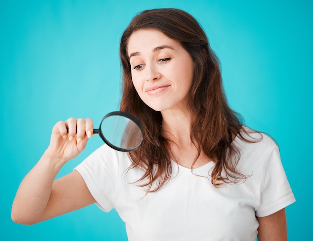 Shes sur le cas Prise de vue en studio d'une jolie jeune femme posant avec une loupe sur un fond bleu