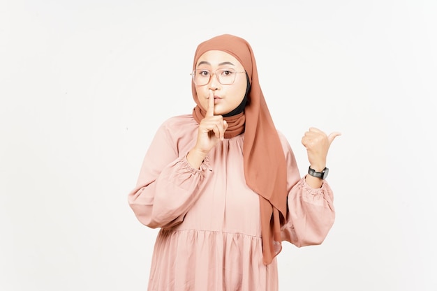 Shh geste présentant et pointant le produit latéral à l'aide du pouce d'une belle femme asiatique portant le hijab