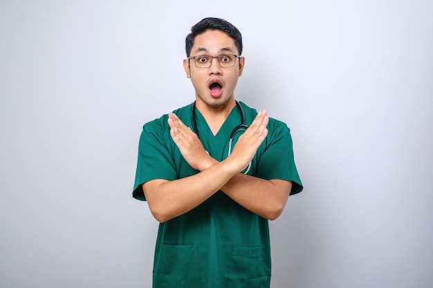 Shockedlooking infirmier médecin en gommage vert croiser les mains dans le panneau d'arrêt interdire ou interdire l'action fronçant les sourcils