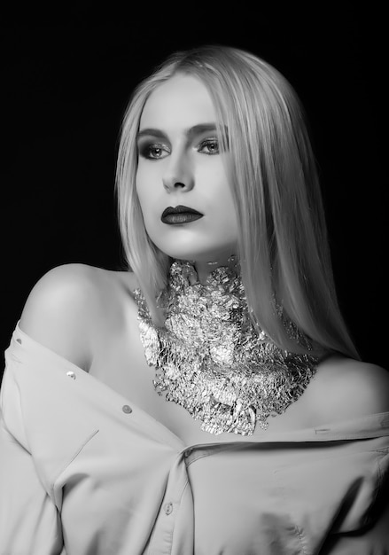 Shooting beauté noir et blanc : jolie mannequin blonde posant en studio avec un maquillage brillant et une feuille sur le cou