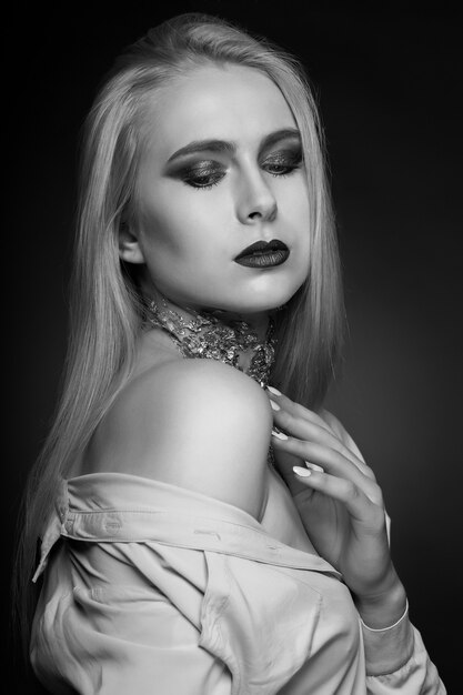 Shooting beauté noir et blanc : mannequin blonde passionnée posant en studio avec un maquillage brillant et une feuille sur le cou