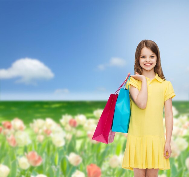 shopping, bonheur et concept de personnes - petite fille souriante en robe jaune avec des sacs à provisions