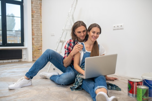 Shopping en ligne. Jeune couple assis sur le sol et à la recherche de quelque chose en ligne