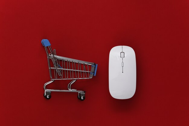 Shopping en ligne. Souris PC et mini caddie avec horloge sur fond rouge. Vue de dessus. Mise à plat