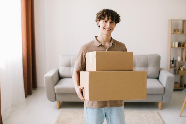 Shopping et livraison Curly Young Man Customer Holding Cardboard Box Posing Smiling To Camera Standing At Home Excited Male Buyer Hugging Colis livré