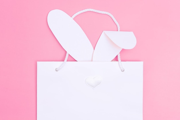 Shopping pour Pâques sac shopping en papier blanc avec des oreilles de lapin blanc sur fond rose Concept cadeaux de Pâques