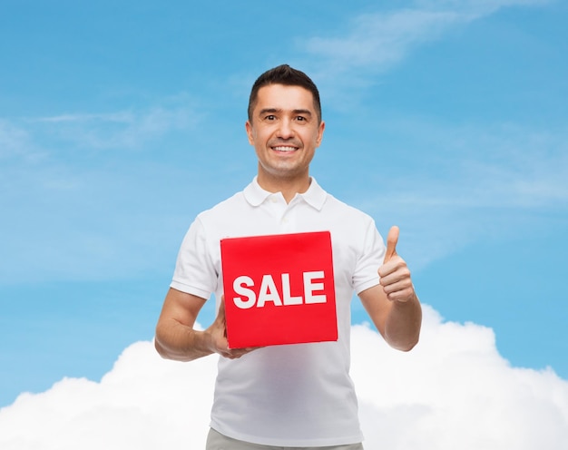 shopping, remise, consumérisme, concept de geste et de personnes - homme souriant avec soupir de vente rouge montrant les pouces vers le haut sur fond bleu ciel et nuage