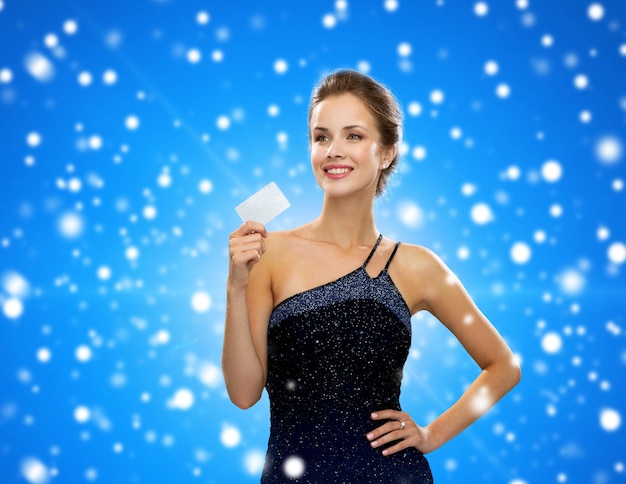 shopping, richesse, vacances et concept de personnes - femme souriante en robe de soirée tenant une carte de crédit sur fond bleu neigeux